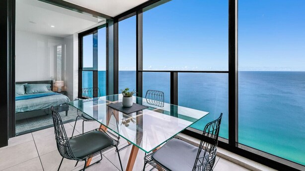 A modern room with a glass table, chairs, a sofa, and a view of the ocean. - Stunning Beachfront level48 with parking /L (Surfers Paradise)