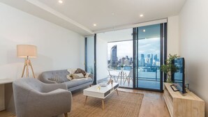 Uma sala de estar moderna com um sofá cinza, uma mesa de centro, um abajur e uma TV sobre um suporte de madeira.