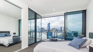 Quarto de hotel moderno com uma cama grande, vista para a cidade e porta de vidro que dá para uma varanda.