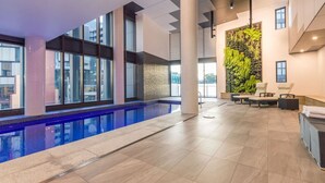 Piscina interna com piso revestido, grandes janelas e parede com jardim vertical.
