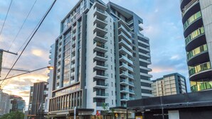 Um hotel de vários andares com design moderno, com varandas em cada pavimento e janelas amplas.