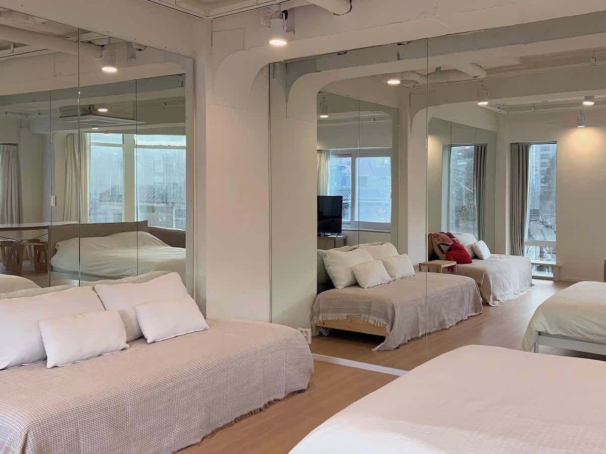 A hotel room with a large mirror, two beds, a TV, and a window.