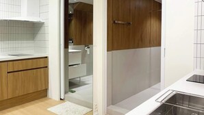 Une cuisine moderne avec un plan de travail blanc, des meubles en bois et une cabine de douche en verre.