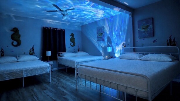 Ein Zimmer mit drei Betten, einem Deckenventilator und einem Wandgemälde.