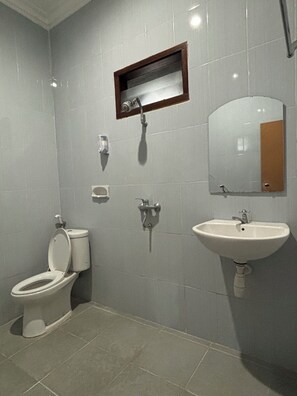 A bathroom with a toilet, sink, mirror, and a small window. - Hotel Prima Asri 153 (Batu)