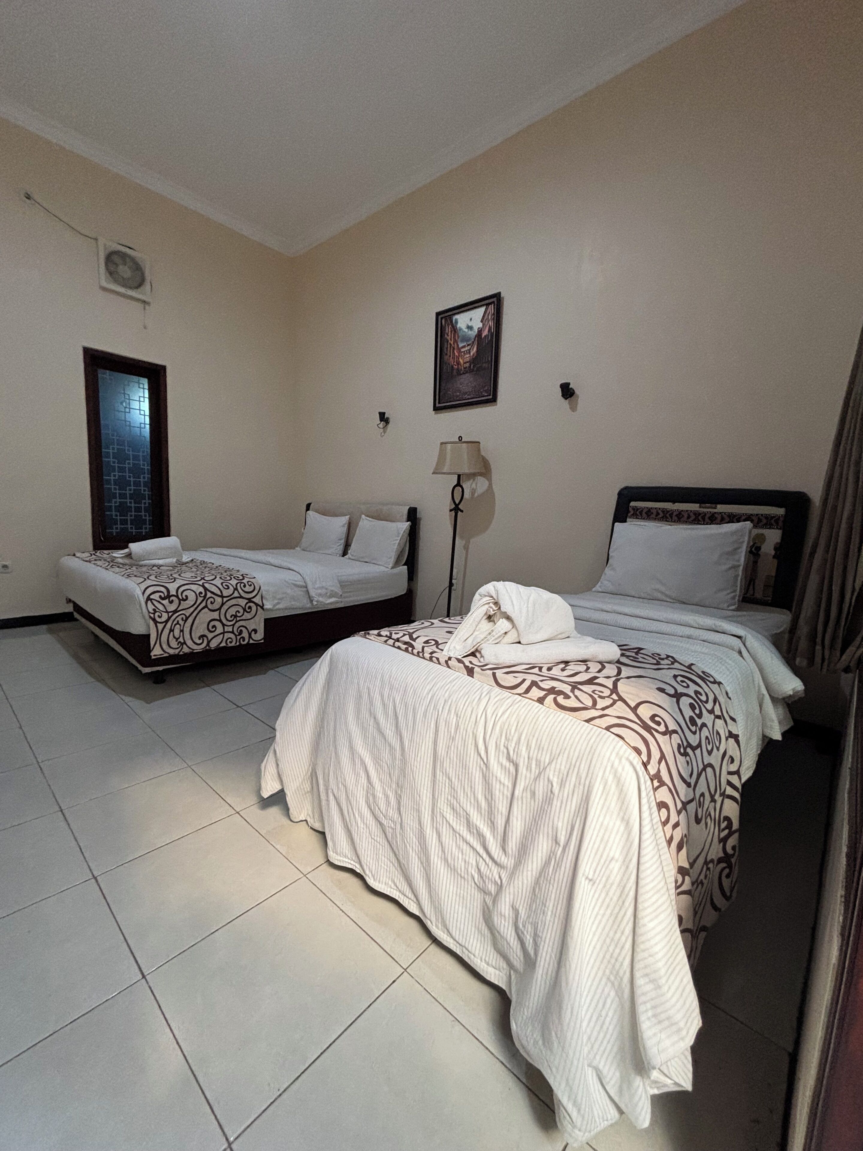 A hotel room with two beds, a clock, a lamp, and a framed picture on the wall.