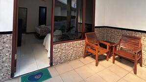 A room with a bed, a small table, and two wooden chairs. There is a door leading to another room. - Hotel Prima Asri 153 (Batu)