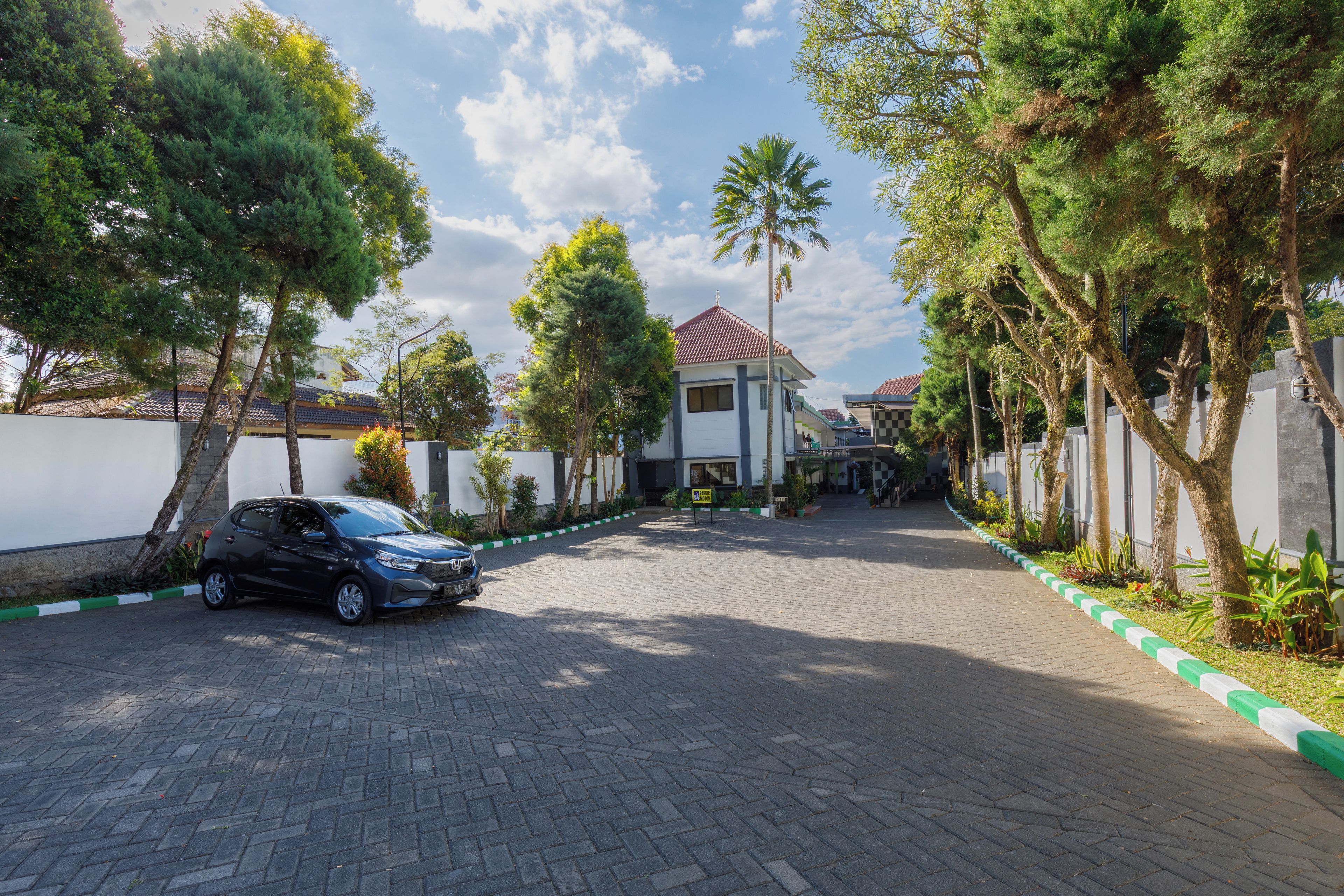 A paved driveway leading to a building with a red-tiled roof, surrounded by trees and a parked car.