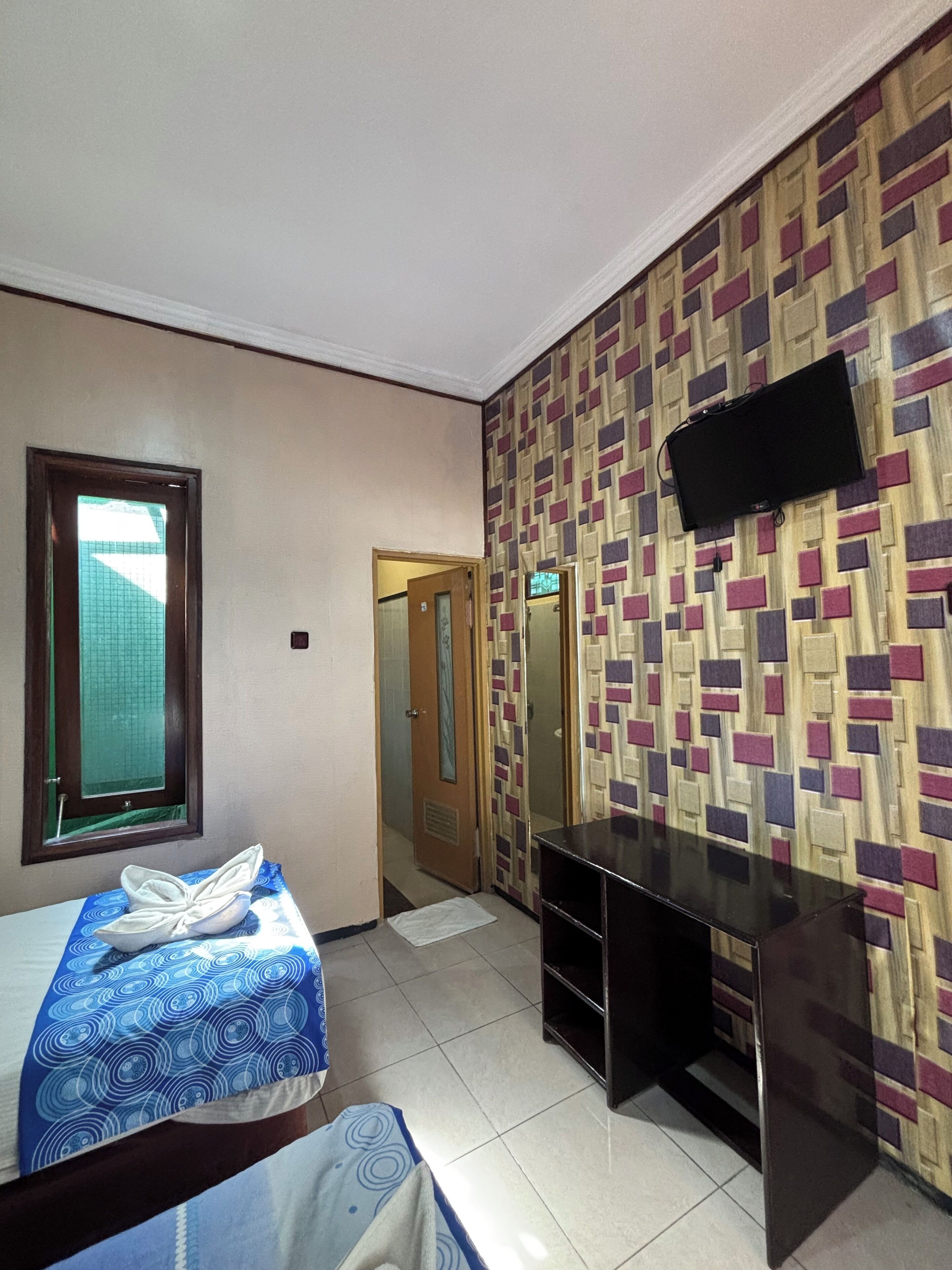 Habitación de hotel con una cama, un escritorio, un televisor montado en la pared y una puerta que da a otra habitación.