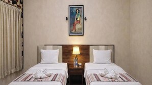 A hotel room with two beds, a headboard with a lamp, a painting on the wall, and a patterned curtain. - Hotel Prima Asri 153 (Batu)