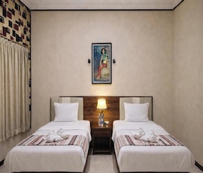 A hotel room with two beds, a headboard with a lamp, a painting on the wall, and a patterned curtain.