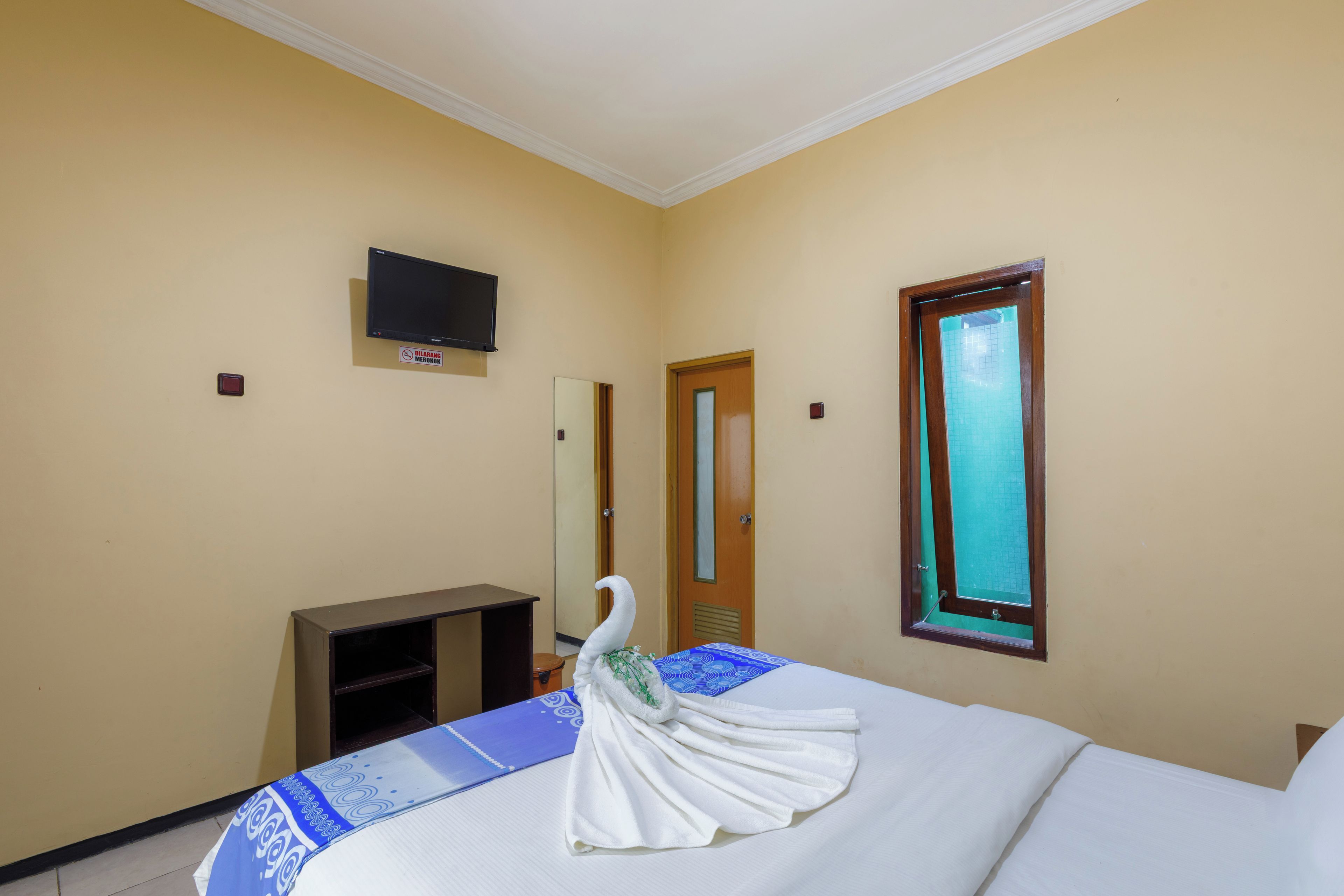 Una habitación de hotel con una cama, un televisor montado en la pared, una puerta y una ventana.
