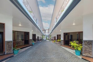 A corridor with a tiled floor, doors on both sides, and potted plants. - Hotel Prima Asri 153 (Batu)