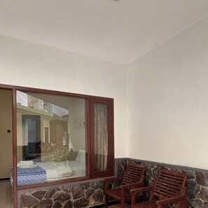 A room with a large sliding glass door, a stone-patterned sofa, and two wooden chairs.