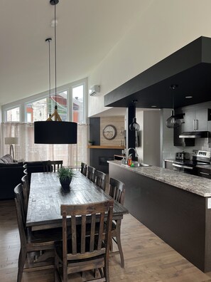 Eine moderne Küche mit Esstisch aus Holz, dunklen Schränken und einer großen Kochinsel.
