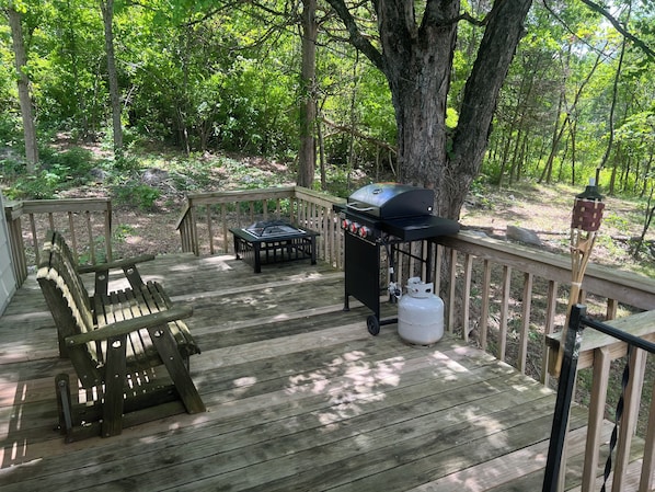 A wooden deck with a grill, a gas tank, and a bench.