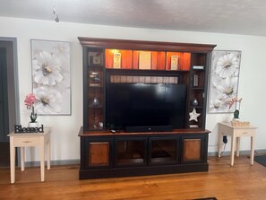 A living room with a dark wood entertainment center, a flat-screen TV, and two side tables with decorative items.