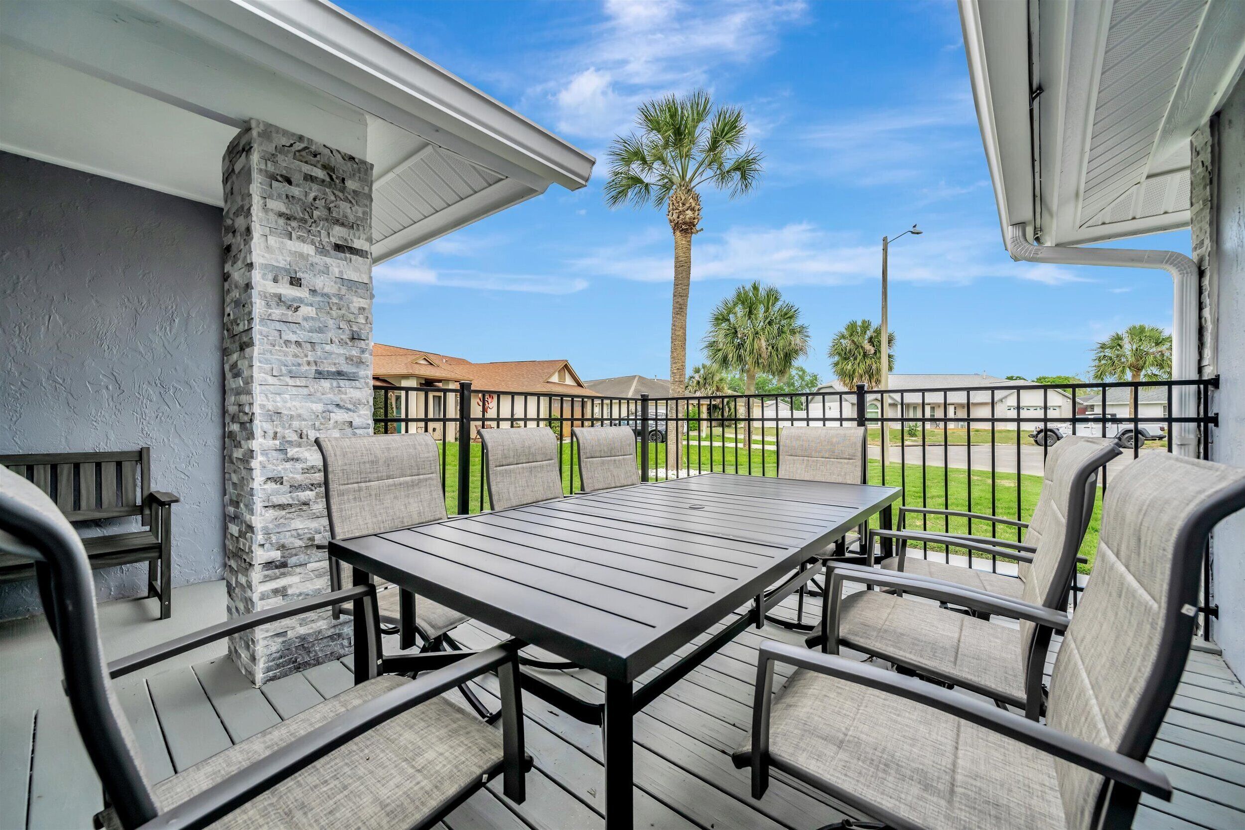 An outdoor patio with a table and chairs, a stone pillar, and a view of palm trees and houses.