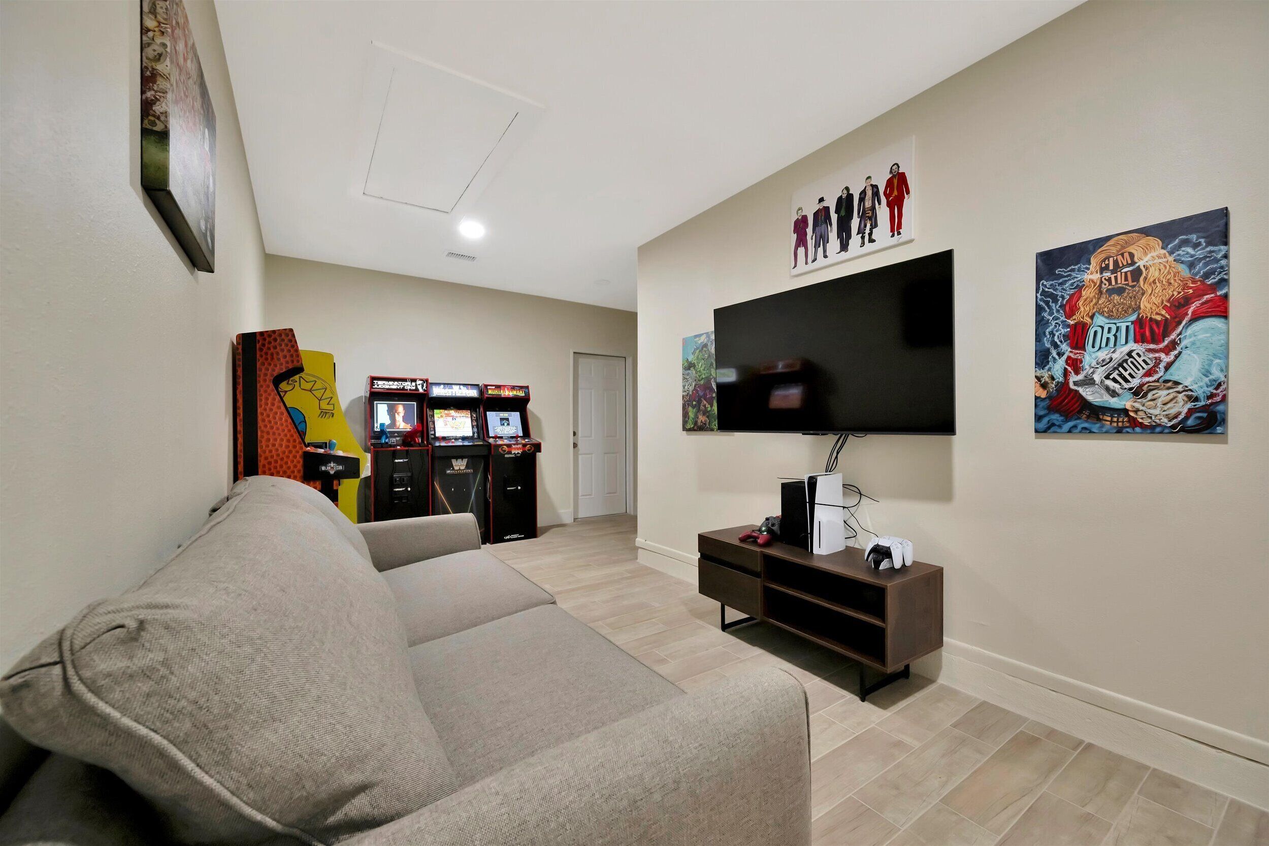 A living room with a sofa, a flat-screen TV, a gaming console, and artwork on the walls.