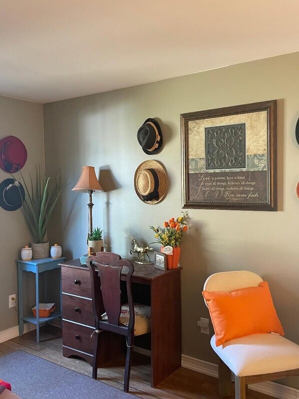 A room with a desk, chair, potted plants, and a framed quote on the wall.
