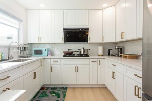 A modern kitchen with white cabinets, a stove, a microwave, and a coffee maker. - Terrific 4-bedroom house with AC in West Covina (West Covina)