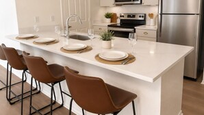 A modern kitchen with a central island, stainless steel appliances, and brown leather chairs.