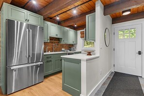 Eine Küche mit grünen Schränken, einem Edelstahlkühlschrank und einer weißen Tür.