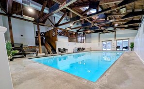 An indoor swimming pool with a concrete floor, wooden beams, and a staircase leading to an upper level. - Remodeled Mountainside Condo w/Pool & Hot Tub! (Stowe)
