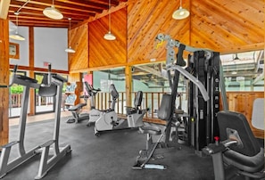A gym with various exercise equipment, wooden ceiling, and large windows. - Remodeled Mountainside Condo w/Pool & Hot Tub! (Stowe)