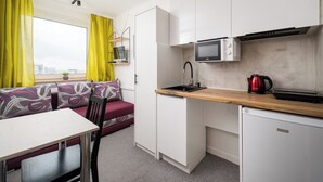 A compact kitchen with a microwave, sink, and a small refrigerator. There is a wooden countertop, a dining table with chairs, and a sofa with a view of the city. - Metro Świętokrzyska Simple Studio (Warszawa)