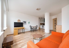 Ein modernes Wohnzimmer mit einer Couch, einem Fernseher, einem Esstisch mit Stühlen und einer Küche im Hintergrund.