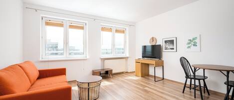 Ein modernes Wohnzimmer mit einer Couch, einem Couchtisch, einem Fernseher, einem Schreibtisch und einem Esstisch mit Stühlen.