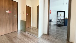 Un pasillo con puertas de madera, un muro con espejo y un comedor con sillas y una estantería.