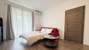 Un dormitorio con cama, una mesita redonda, un armario y una ventana con cortinas.