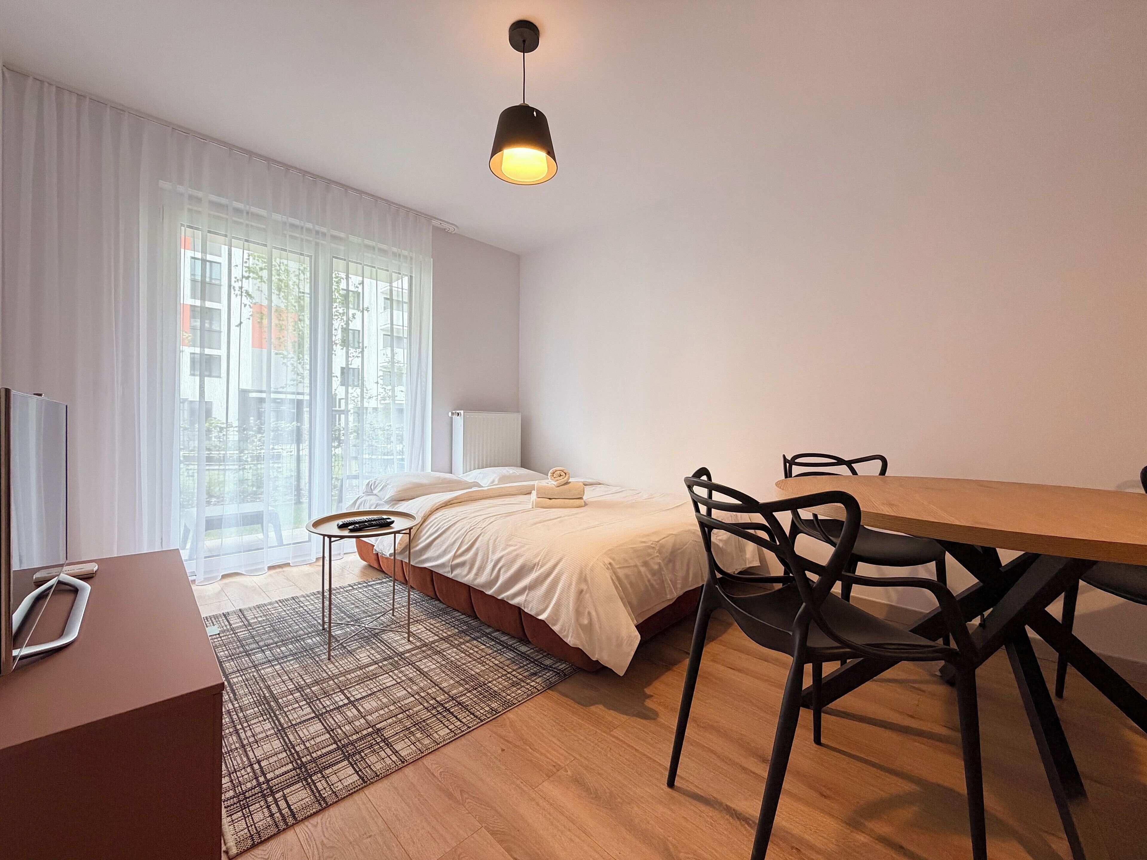 Un dormitorio moderno con cama, mesita de noche y un espacio de escritorio con sillas.