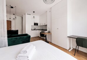 Ein modernes Hotelzimmer mit Bett, Schreibtisch, Sessel, einer Küchenzeile und einem grünen Sofa.