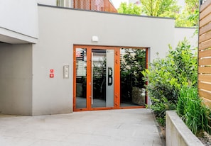 Ein Gebäudeeingang mit Glastür, Brandmelder und einem kleinen Fenster.