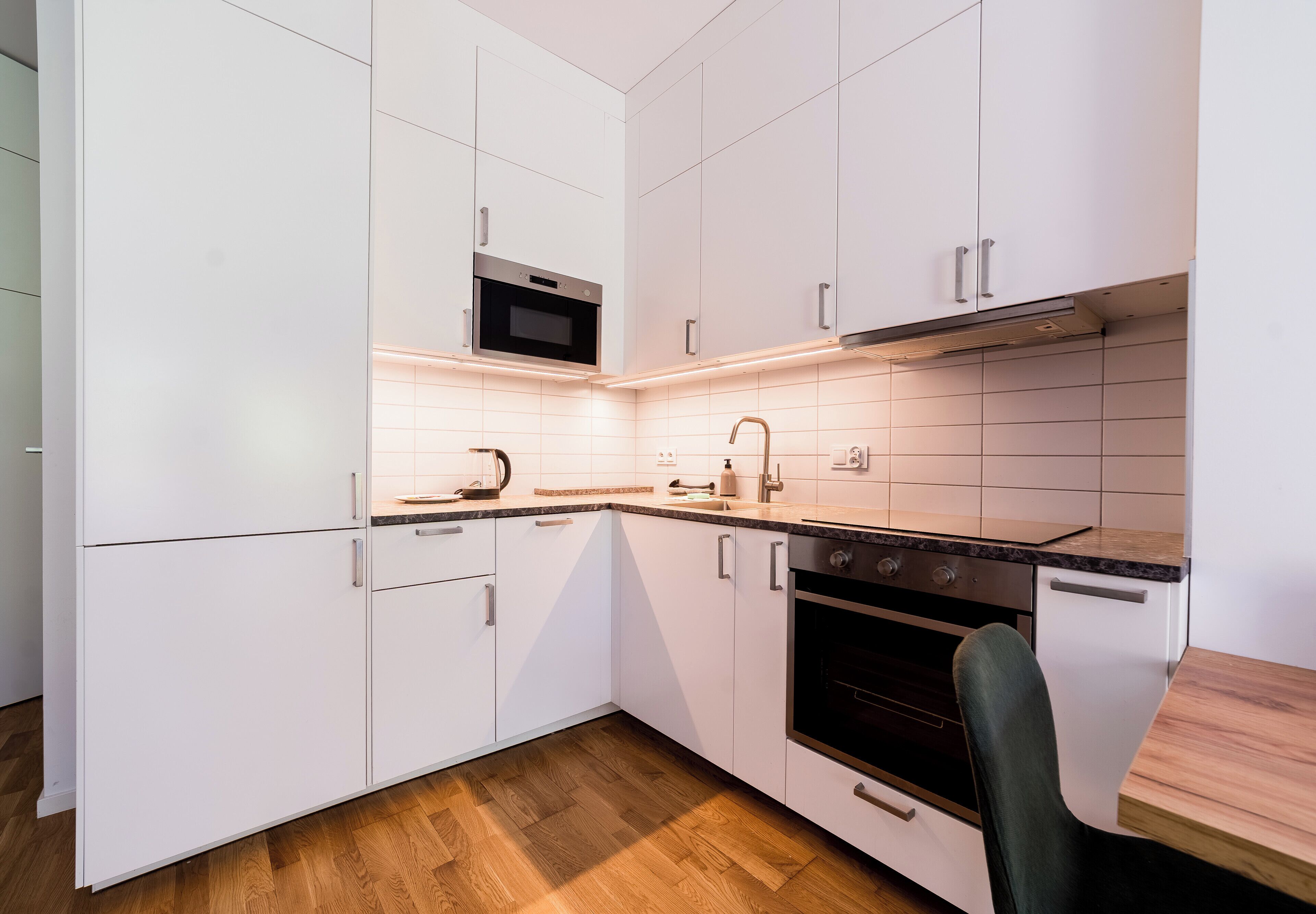A modern kitchen with white cabinets, a microwave, an oven, and a wooden dining table.