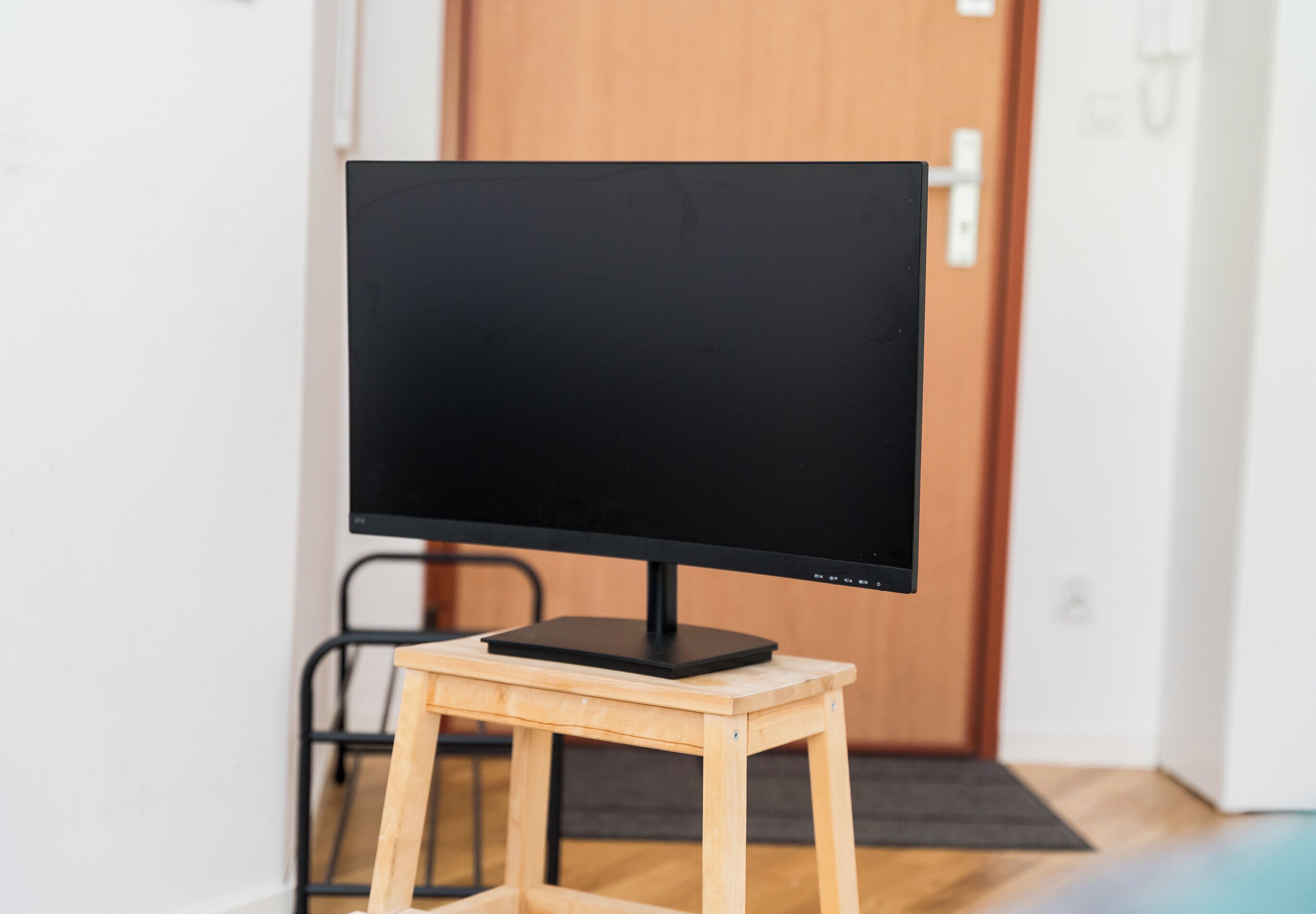 Un televisor de pantalla plana sobre un soporte de madera en una habitación con una puerta de madera y un felpudo negro al fondo.