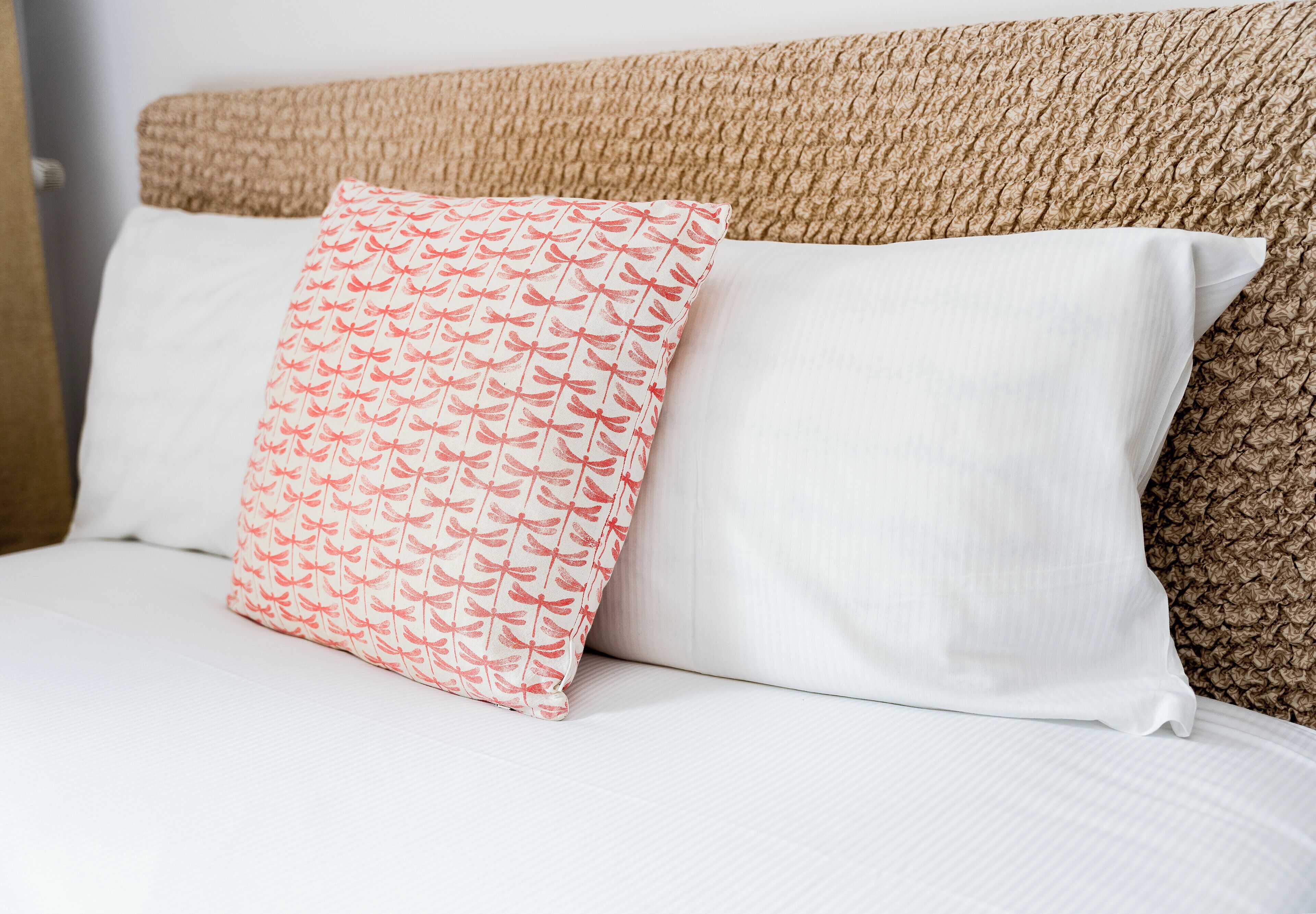 A bed with two pillows, one patterned and one plain, and a textured headboard.