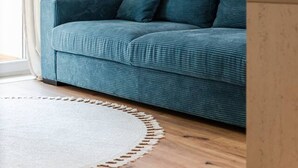 En turkos soffa placerad framför en vit tegelvägg, ett trägolv och en beige matta.