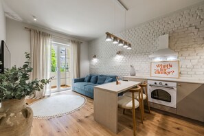 A modern kitchen with a white brick wall, a blue sofa, a dining table with chairs, and a sign asking 'What's for dinner?'. - The Homey Flat Stylish 2BR City Apartment (Tirana)