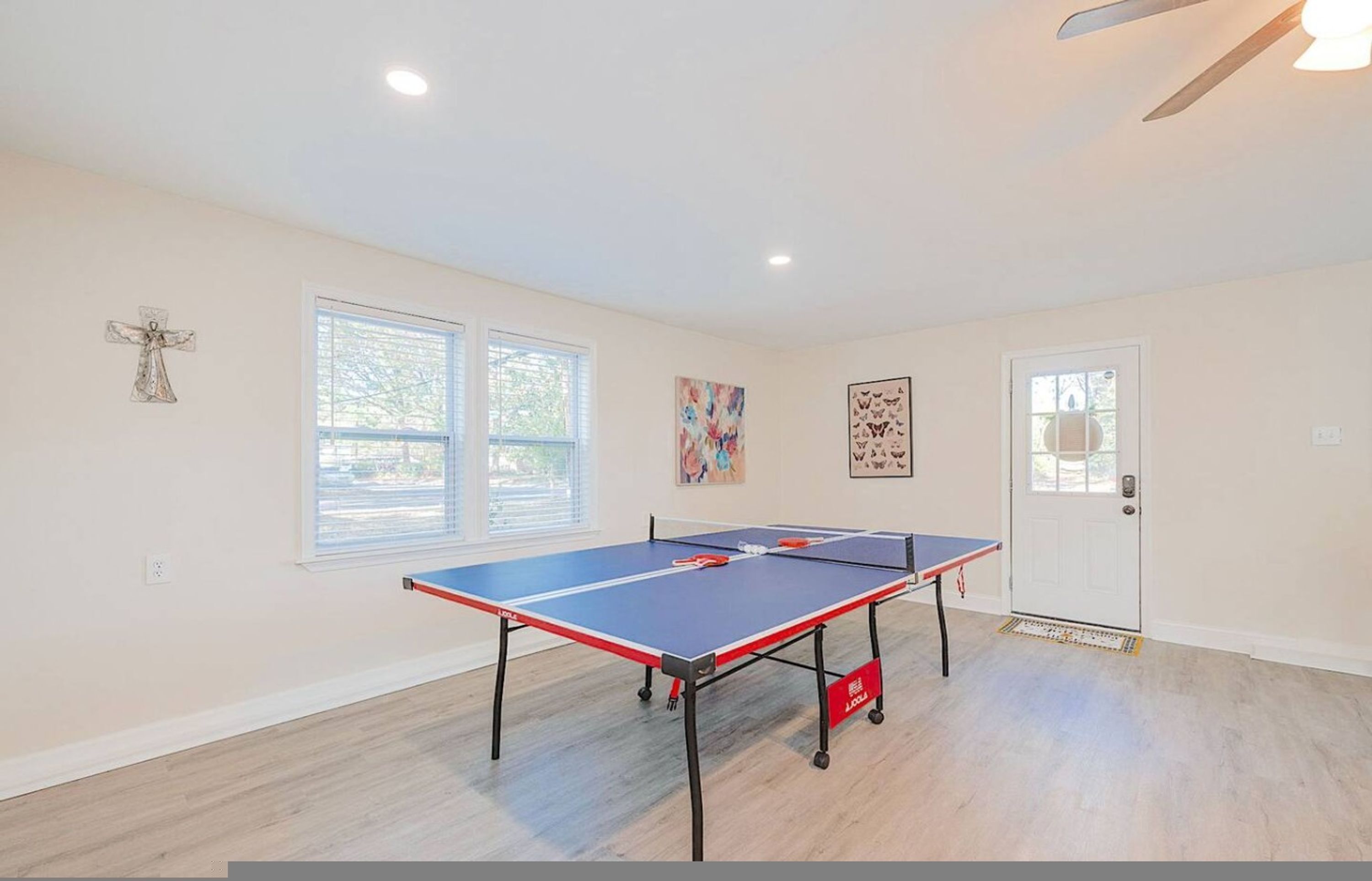 A room with a ping pong table, two windows, a door, and a ceiling fan.