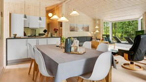 Ein modernes Interieur mit Essbereich, Küche und großen Fenstern mit Blick ins Freie.
