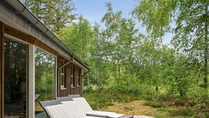 Eine Holzterrasse mit zwei Liegestühlen und einer Glastür, die zu einem Raum führt.