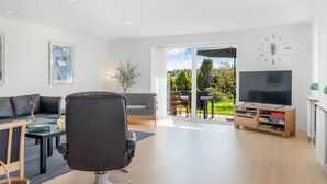 Un soggiorno moderno con un divano, una poltrona da ufficio nera, un mobile TV con televisore a schermo piatto e un'area pranzo con tavolo e sedie.