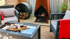 A cozy outdoor seating area with wicker furniture, a fire pit, and a table with snacks and drinks. - Tully Cottage - a home among the gum trees (Break O'Day)