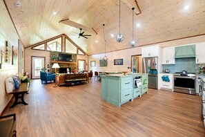 A spacious living area with a high ceiling, wooden floors, a central seating area with a sofa and armchairs, a kitchen with modern appliances, and a dining area. - The Deerpath- Wheelchair friendly-wifi- putt putt and more! (Morganton)