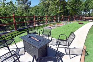 Une terrasse extérieure avec une table et des chaises autour d’un foyer, le tout entouré d’une clôture en bois et d’une pelouse.
