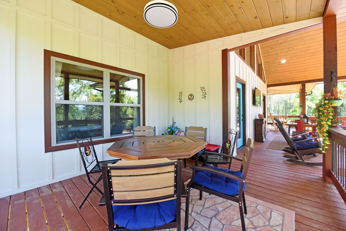 A covered patio with a wooden table and chairs, a stone floor, and a view of the outdoors.